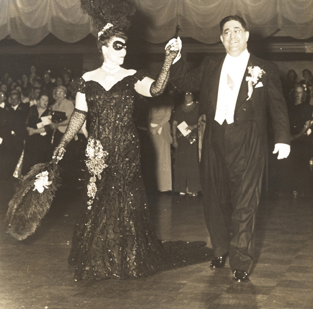 Captain Aminthe Nungesser, masked and gowned with an ostrich-plume fan, escorts King Roger Joseph Barba Sr. in white tie at the 1949 Iris ball